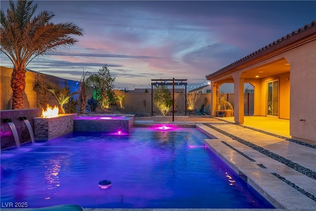 pool at dusk with a fenced backyard, a fire pit, a patio area, and a pool with connected hot tub