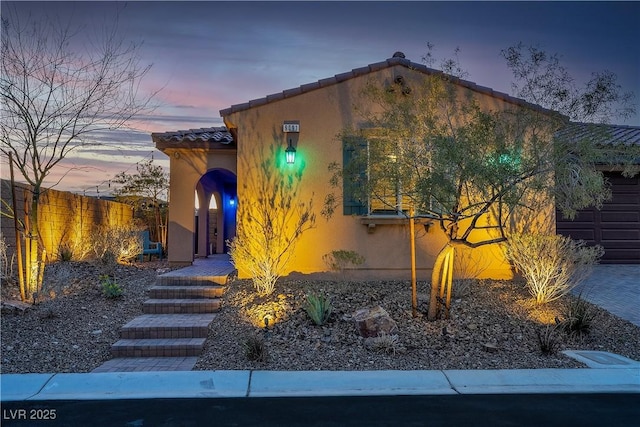 mediterranean / spanish house featuring a tiled roof, stucco siding, and fence