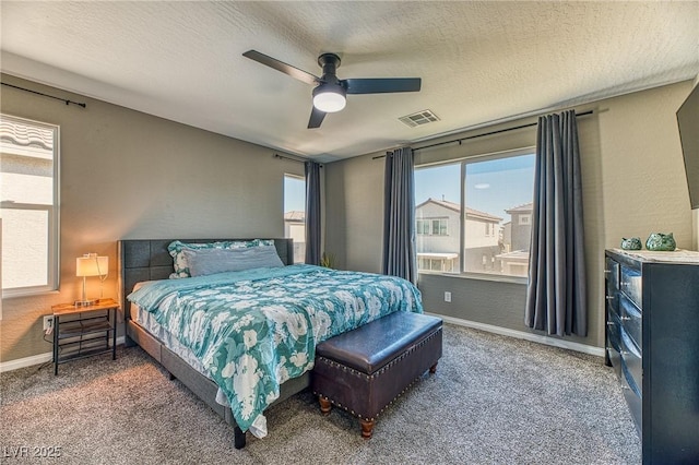 bedroom with a textured ceiling, ceiling fan, carpet floors, baseboards, and visible vents