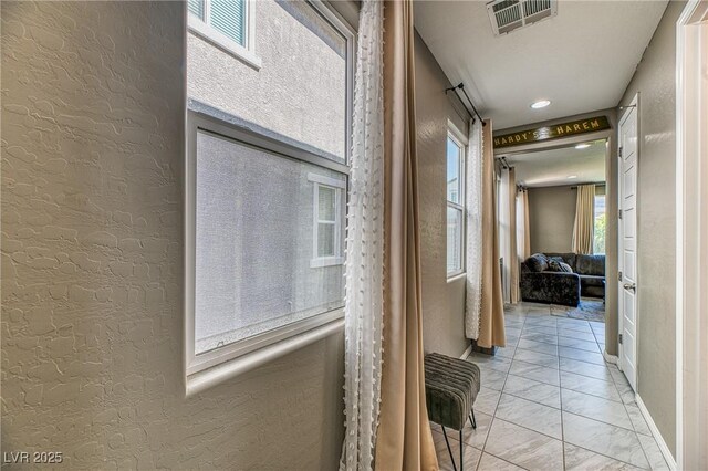 corridor with marble finish floor, baseboards, a textured wall, and visible vents
