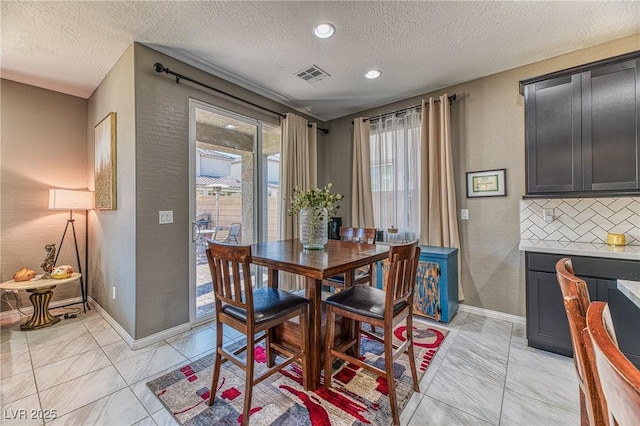 dining room with marble finish floor, a textured wall, visible vents, baseboards, and a textured ceiling