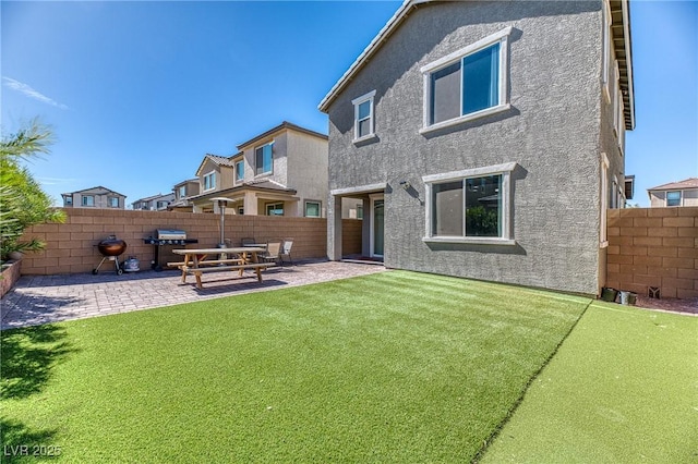 rear view of house with stucco siding, a patio, a fenced backyard, and a lawn