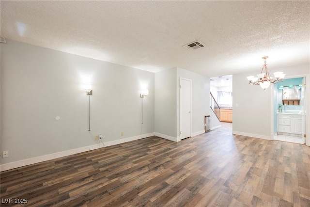 empty room featuring stairs, wood finished floors, a textured ceiling, a chandelier, and visible vents