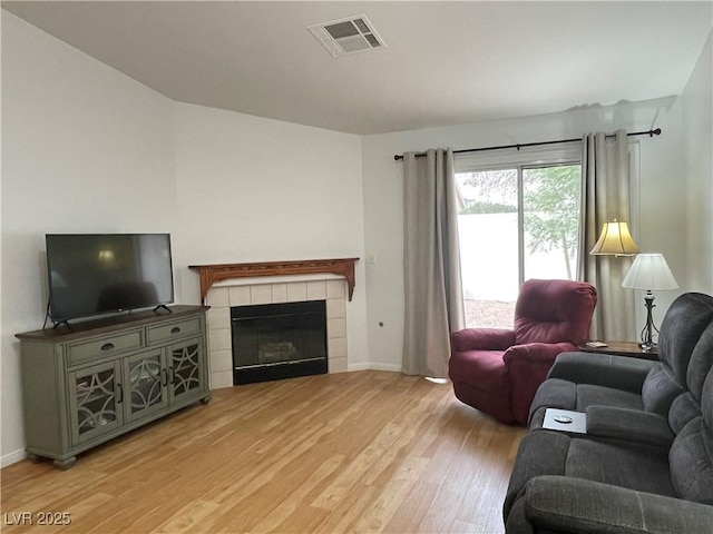 living room featuring a tile fireplace, light wood-type flooring, visible vents, and baseboards