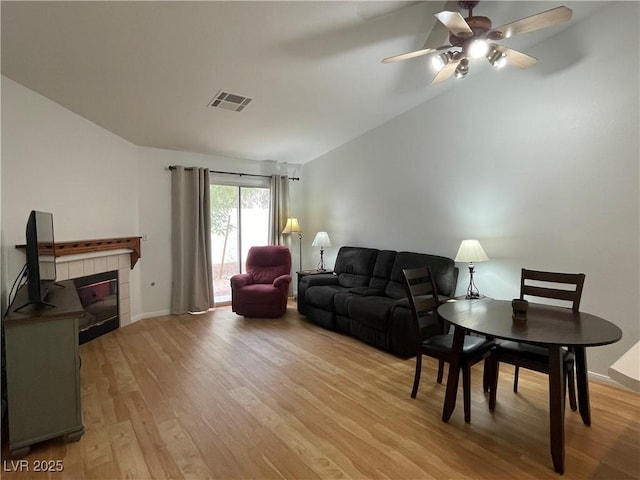living area featuring light wood-type flooring, vaulted ceiling, visible vents, a ceiling fan, and a fireplace