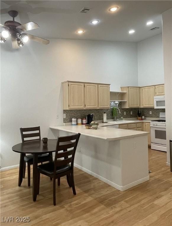 kitchen featuring a peninsula, light brown cabinets, white appliances, and light countertops