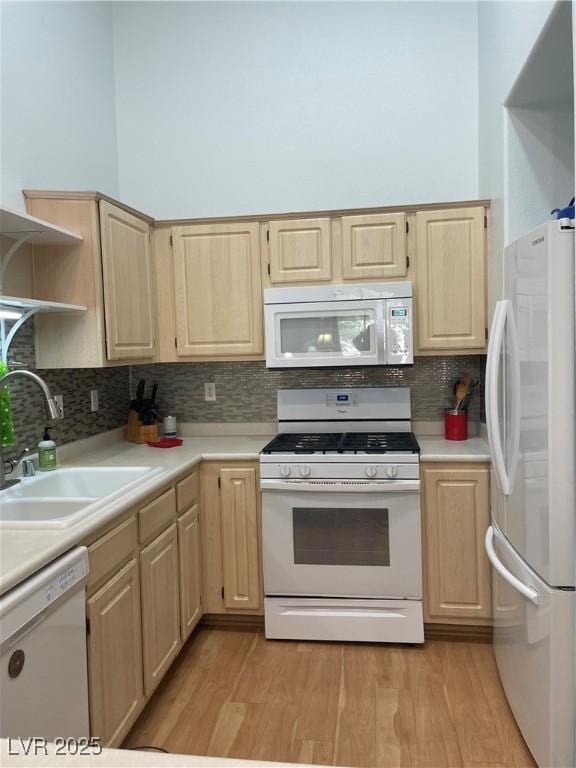 kitchen with light wood finished floors, light brown cabinetry, light countertops, a sink, and white appliances