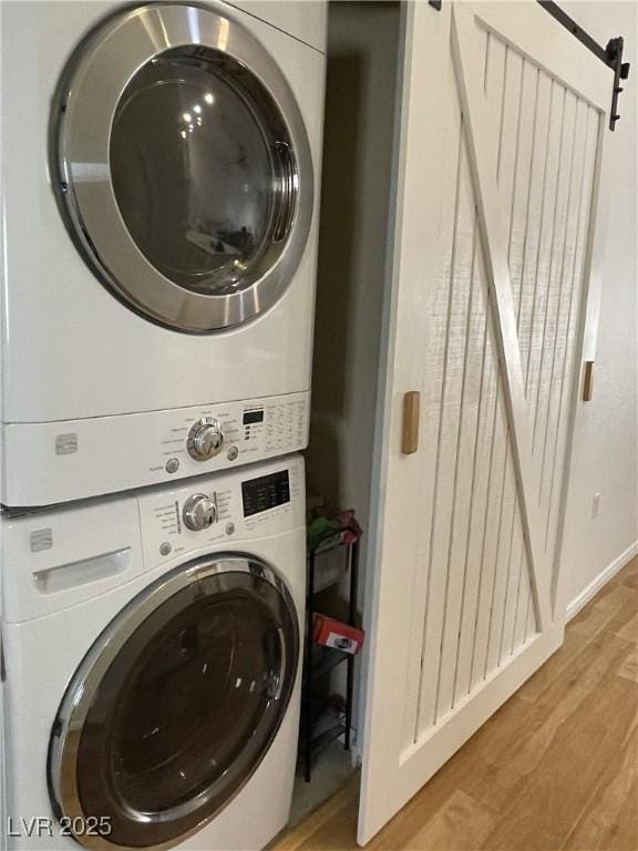 clothes washing area featuring a barn door, light wood-style floors, and stacked washing maching and dryer