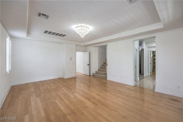 spare room with visible vents, a raised ceiling, an inviting chandelier, and stairway
