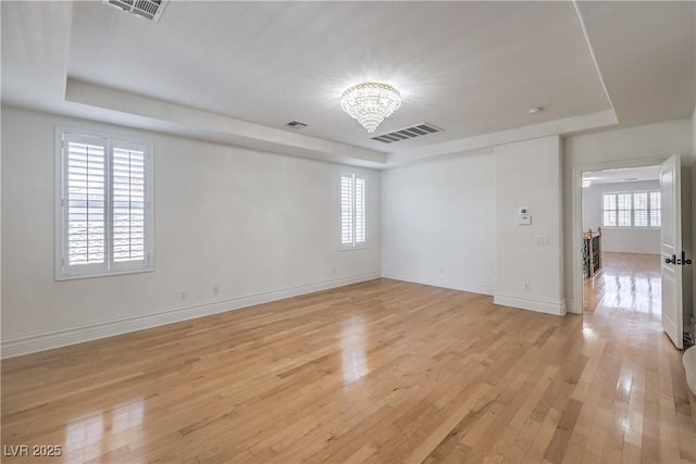 unfurnished room with an inviting chandelier, visible vents, a raised ceiling, and light wood-type flooring