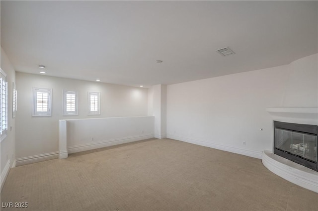 basement featuring light colored carpet, visible vents, baseboards, a glass covered fireplace, and recessed lighting