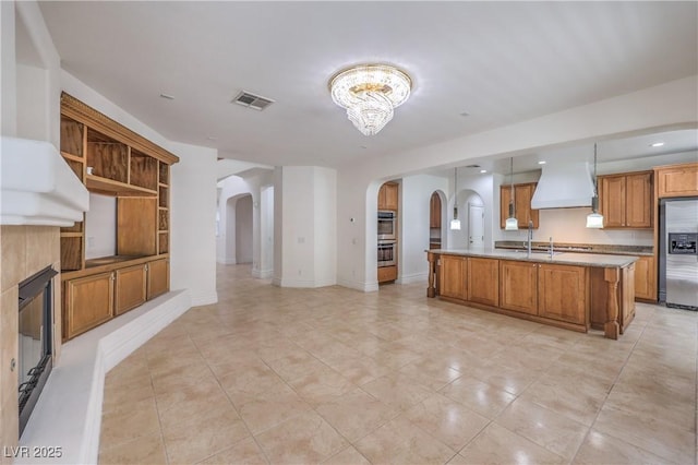 kitchen featuring stainless steel appliances, custom range hood, visible vents, arched walkways, and open floor plan