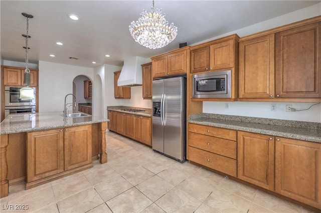 kitchen featuring brown cabinetry, custom range hood, appliances with stainless steel finishes, and a sink