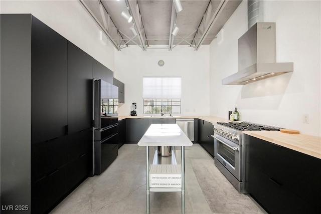 kitchen featuring modern cabinets, wall chimney range hood, light countertops, dark cabinets, and appliances with stainless steel finishes