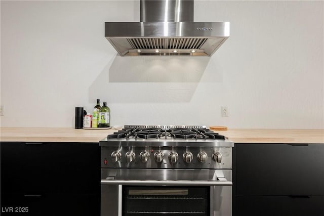 kitchen with dark cabinets, wall chimney exhaust hood, and stainless steel range