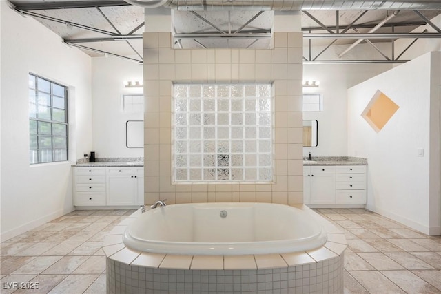 full bathroom featuring baseboards, two vanities, and a bath