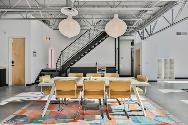 dining space featuring visible vents, concrete flooring, baseboards, a high ceiling, and stairway