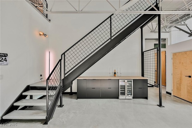stairway with a towering ceiling, concrete floors, a bar, and wine cooler