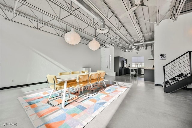 dining area with stairs, concrete flooring, baseboards, and a towering ceiling