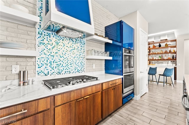 103 Reflection Cove Dr, Henderson, NV 89011 - kitchen with open shelves, brown cabinets, stainless steel appliances, light wood finished floors, and custom range hood