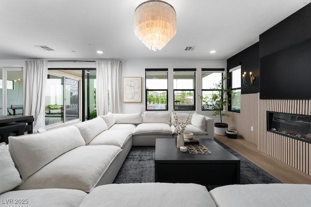 living room featuring a glass covered fireplace, wood finished floors, visible vents, and an inviting chandelier
