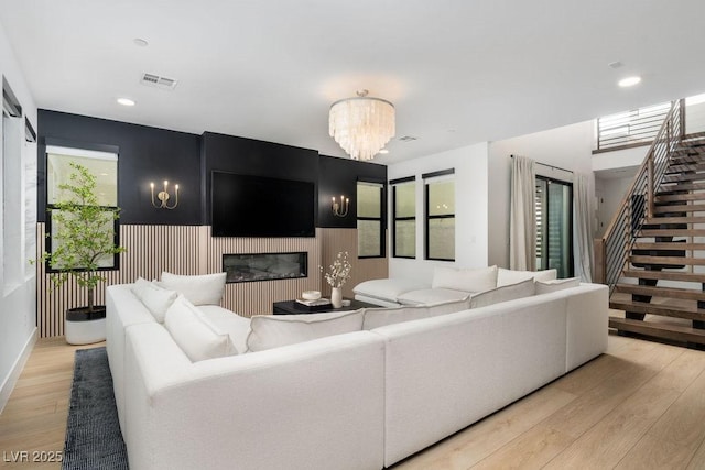living room with recessed lighting, stairway, light wood finished floors, visible vents, and a glass covered fireplace