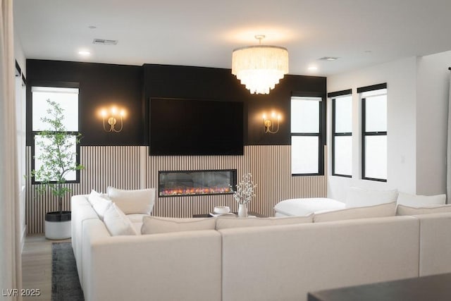 living room featuring a glass covered fireplace, wood finished floors, visible vents, and recessed lighting