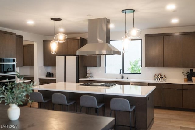 kitchen featuring cooktop, a kitchen bar, island range hood, and dark brown cabinetry