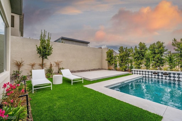 pool at dusk with fence, a lawn, a fenced in pool, and a patio area