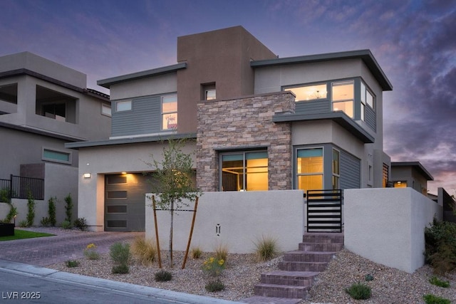 contemporary house featuring a garage, driveway, stone siding, and stucco siding