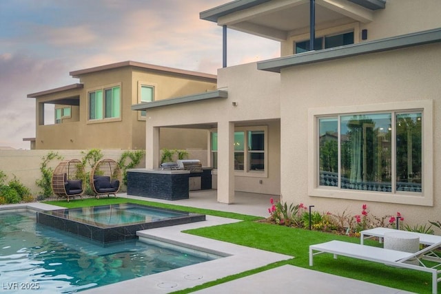 rear view of house with fence, a patio, area for grilling, stucco siding, and a pool with connected hot tub