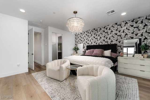 bedroom with baseboards, visible vents, an accent wall, a notable chandelier, and wallpapered walls
