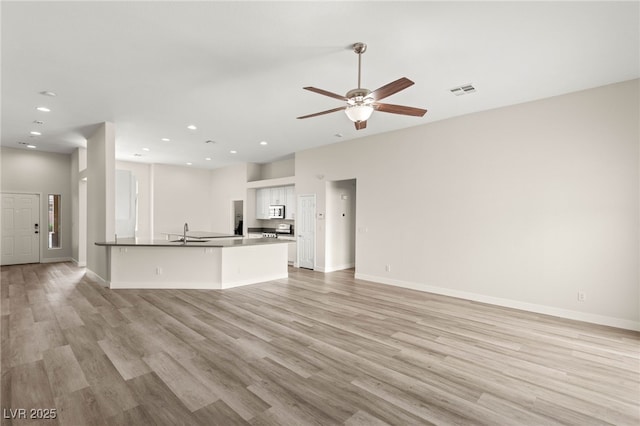 unfurnished living room featuring light wood finished floors, baseboards, and a sink