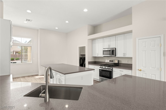 kitchen with a center island, a sink, washer / dryer, white cabinets, and appliances with stainless steel finishes