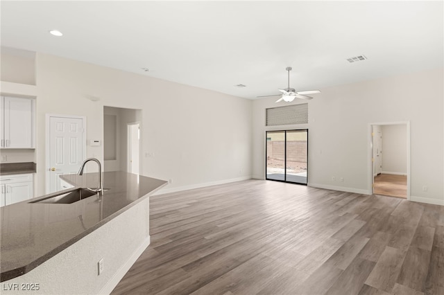 unfurnished living room featuring a sink, light wood-type flooring, baseboards, visible vents, and a ceiling fan