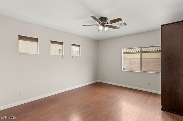 unfurnished room with ceiling fan, a wealth of natural light, wood finished floors, and visible vents