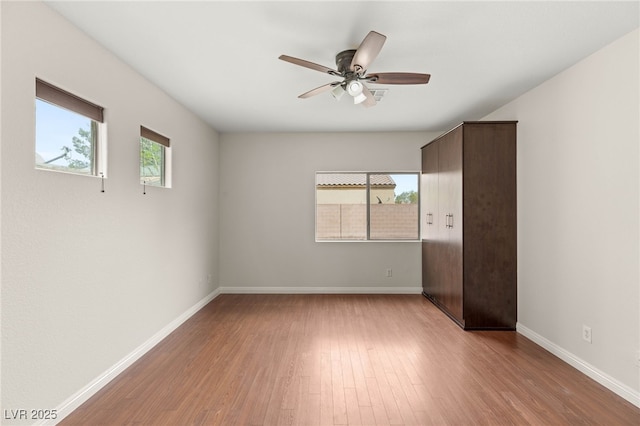 unfurnished bedroom featuring ceiling fan, baseboards, wood finished floors, and multiple windows