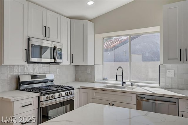 kitchen featuring white cabinets, light stone counters, a sink, decorative backsplash, and appliances with stainless steel finishes