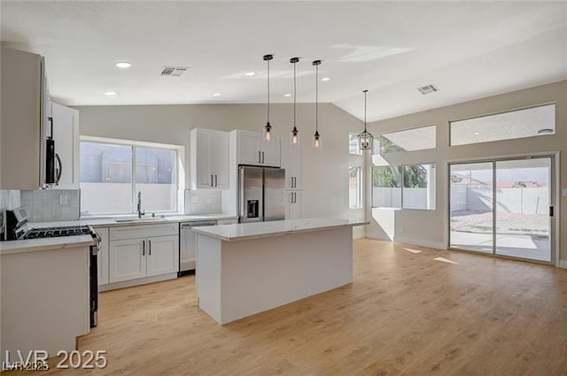 kitchen featuring lofted ceiling, stainless steel appliances, visible vents, a sink, and a kitchen island