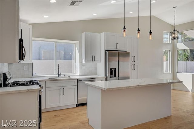 kitchen with a sink, stainless steel appliances, decorative light fixtures, backsplash, and visible vents