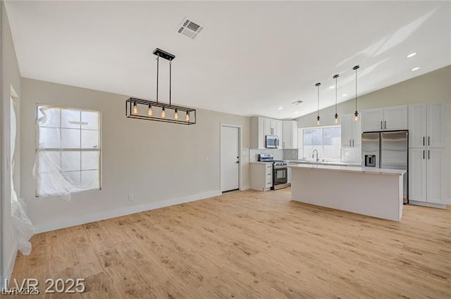 kitchen with light wood finished floors, a center island, lofted ceiling, light countertops, and appliances with stainless steel finishes