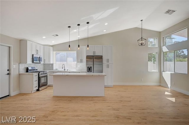 kitchen with light countertops, backsplash, appliances with stainless steel finishes, visible vents, and a kitchen island