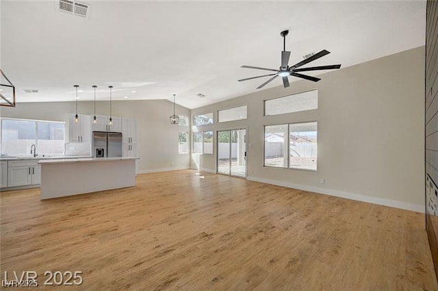 unfurnished living room featuring a ceiling fan, light wood-style flooring, baseboards, lofted ceiling, and visible vents