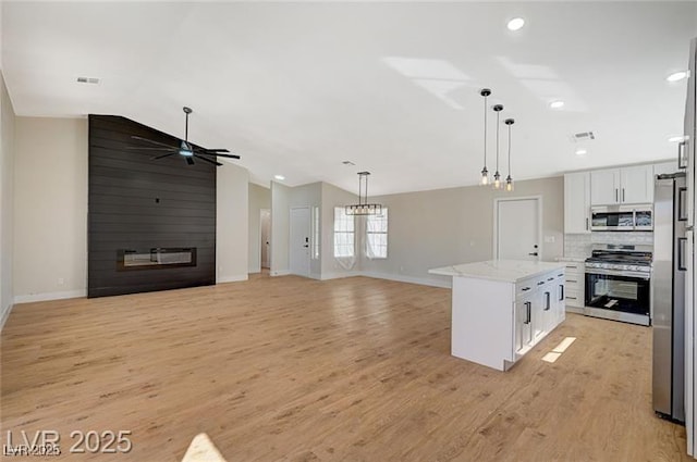 kitchen featuring vaulted ceiling, open floor plan, stainless steel appliances, baseboards, and white cabinetry