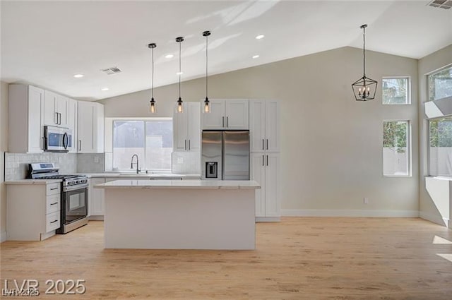 kitchen with stainless steel appliances, light wood-style flooring, a sink, backsplash, and a kitchen island