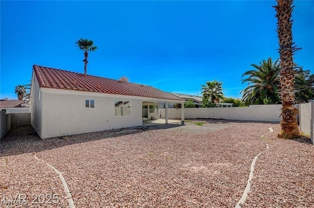 rear view of property featuring a tile roof, a fenced backyard, a patio area, and stucco siding
