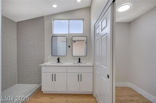 full bath featuring vaulted ceiling, wood finished floors, a sink, and double vanity