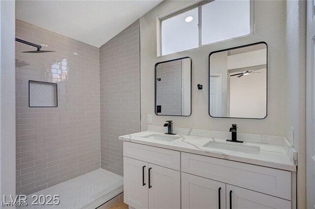 bathroom featuring lofted ceiling, tiled shower, and a sink