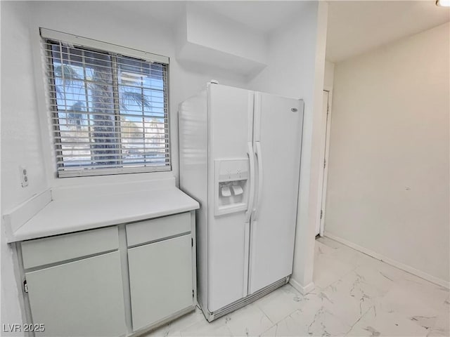 kitchen with marble finish floor, light countertops, white refrigerator with ice dispenser, and baseboards
