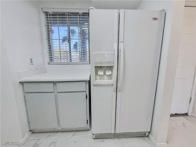 kitchen with marble finish floor, light countertops, white refrigerator with ice dispenser, and baseboards